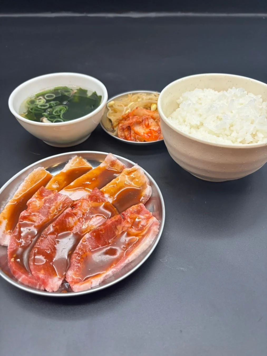 タレに漬け込まれた生肉、白いご飯、ワカメスープ、キムチとナムルの小鉢が並び、焼肉定食のような構成