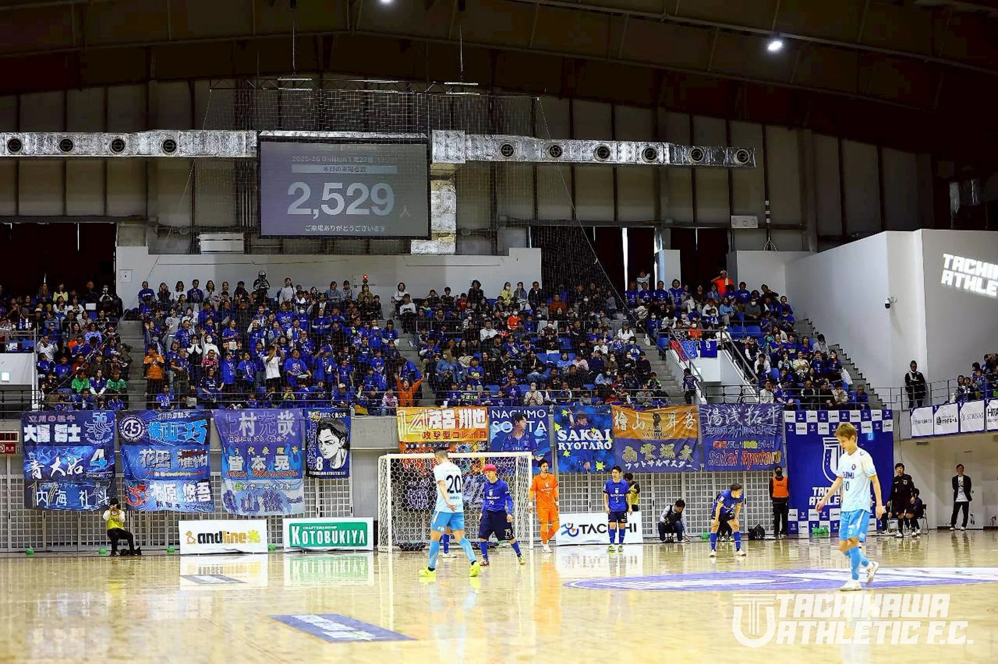 フットサル試合中の屋内アリーナで電光掲示板に入場者数2,529人が表示されている