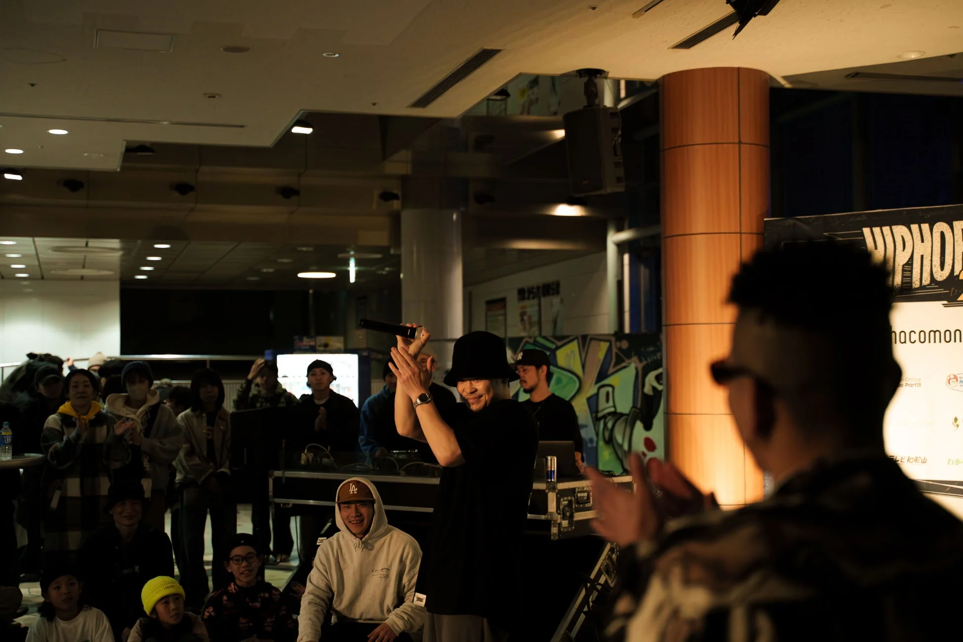 屋内でDJがマイクを持ち、観客からの拍手に応えている