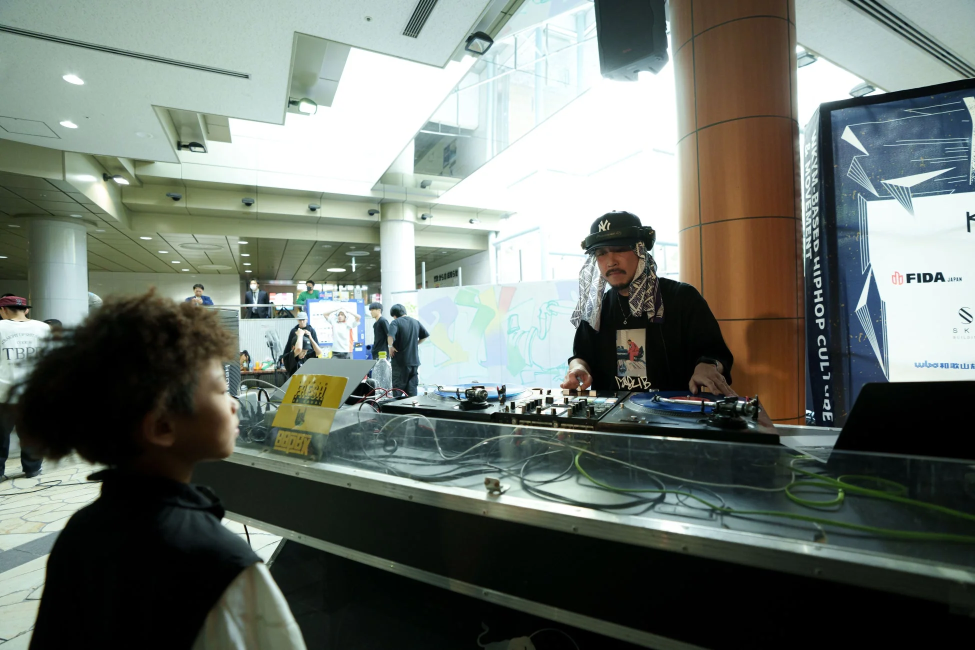 DJがターンテーブルを操作し、観客の子供がその様子を見ているイベント風景