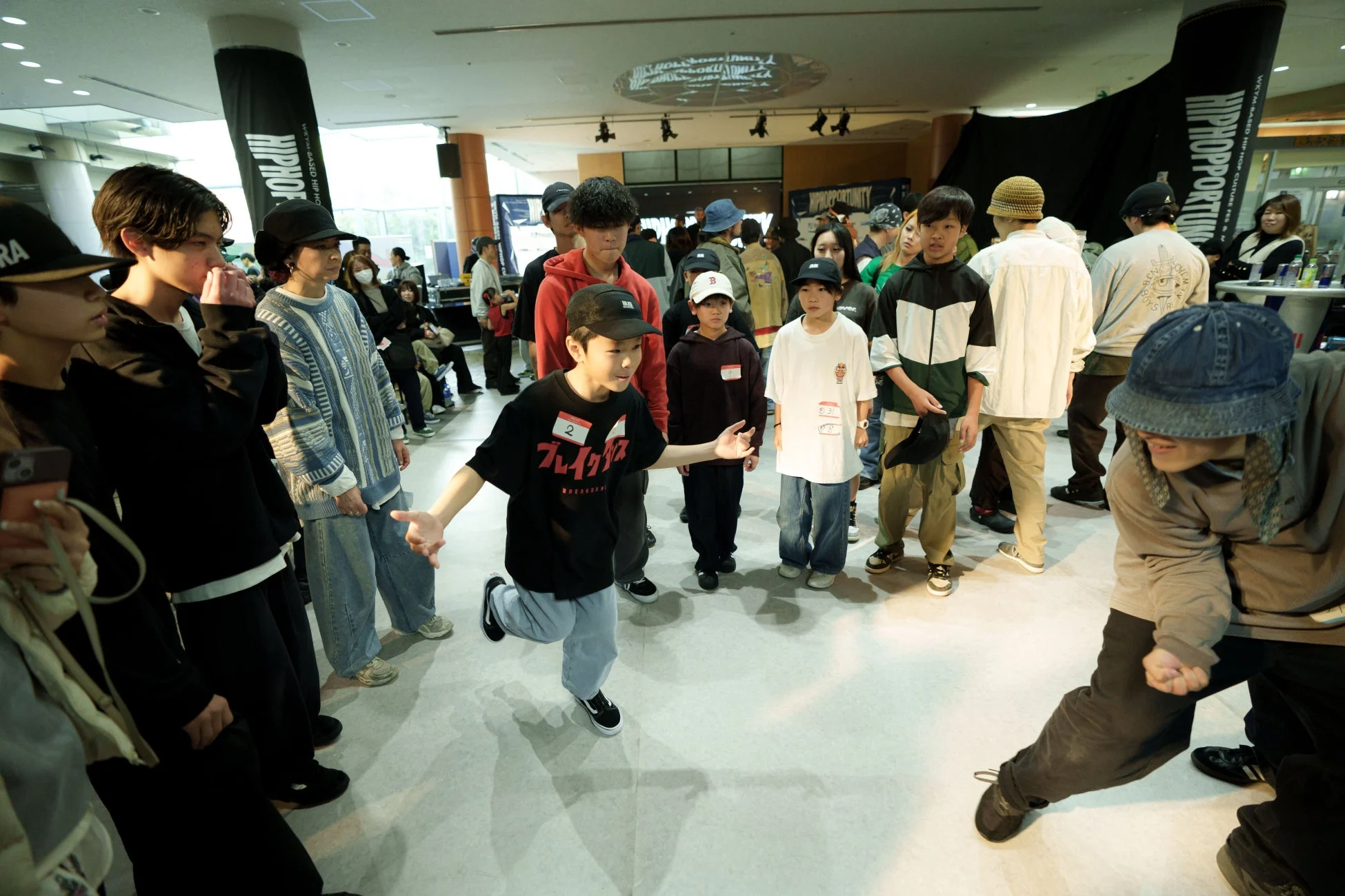 屋内のヒップホップダンスイベントで、多くの若者や子供たちが集まっている