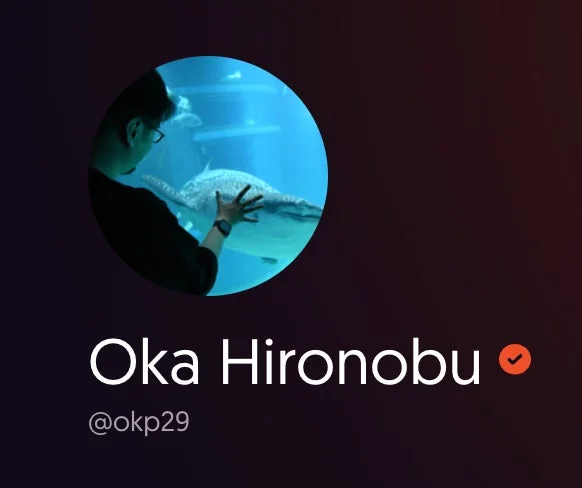 水族館の青い水槽の中で、男性がジンベエザメのような大型の海洋生物に触れているプロフィール画像