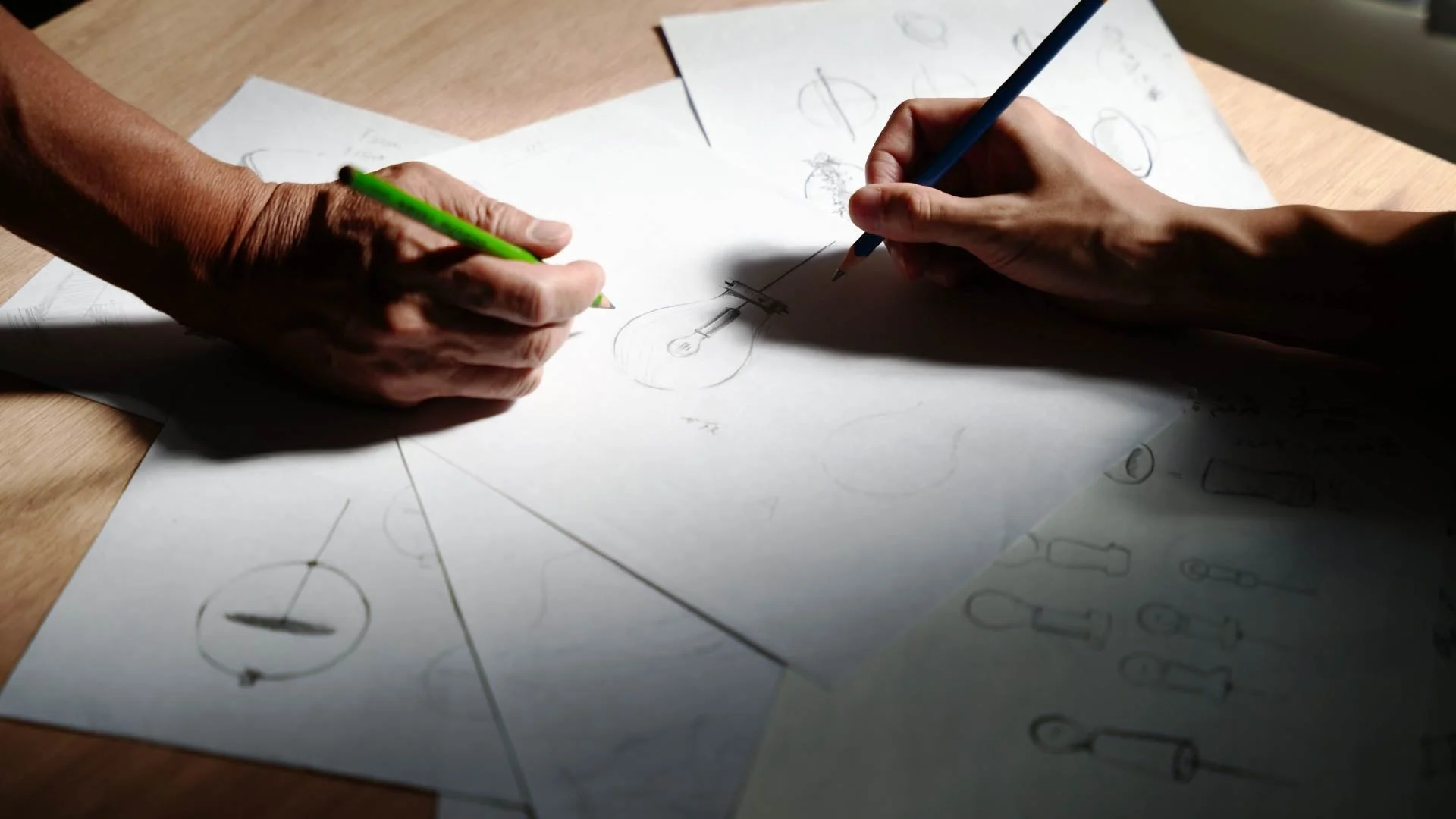 木製のテーブルに広げられた紙の上で、電球などのデザインスケッチを描く手