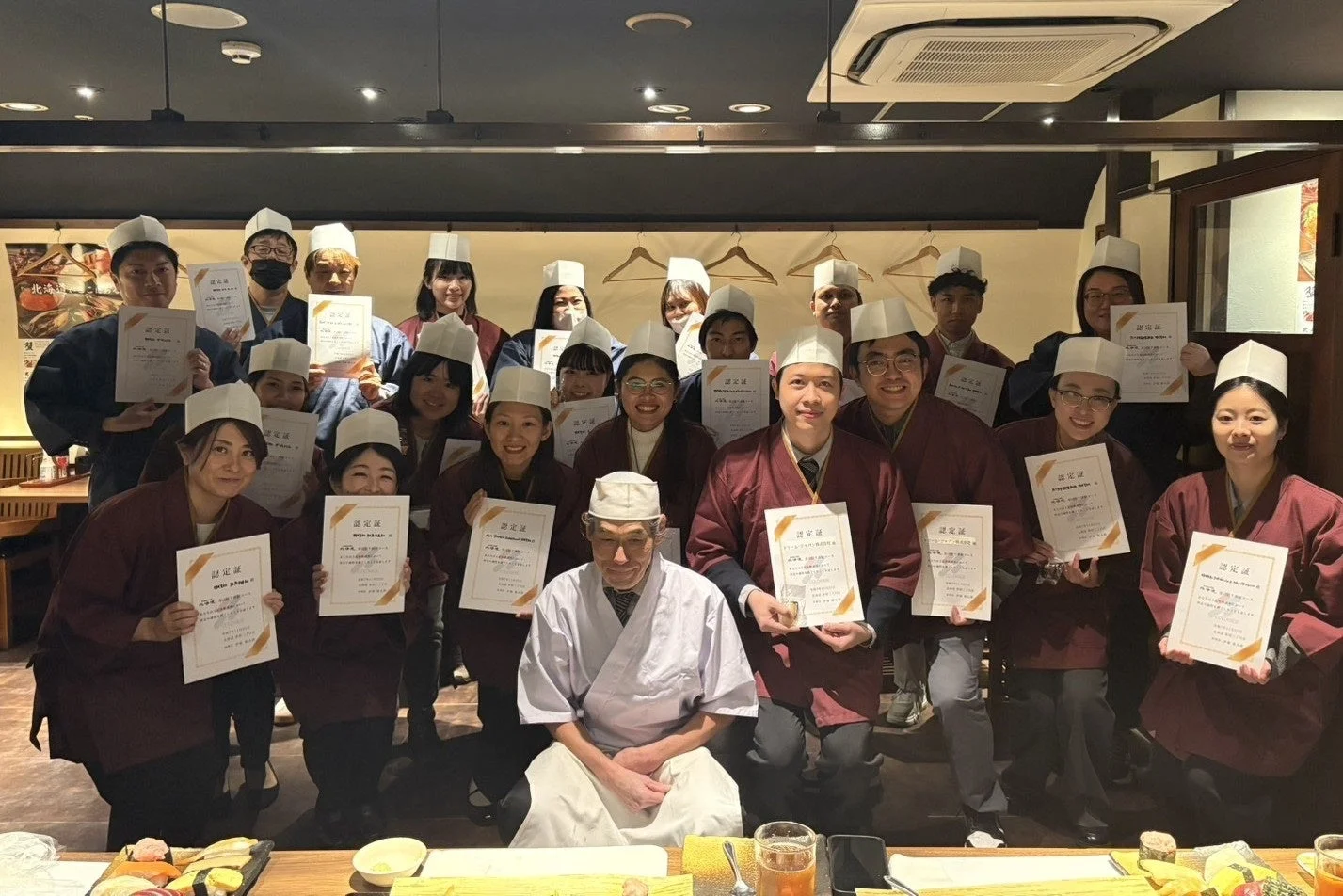 日本食レストランで、多くの人々が「認定証」を手に笑顔で集合写真を撮っている
