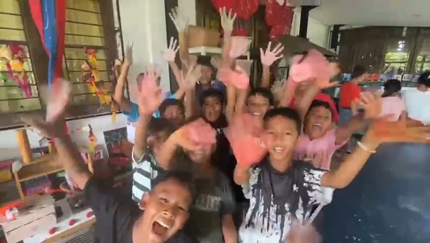 屋内で多くの子供たちが手を高く上げて笑顔で歓声を上げている様子を捉えた画像です。皆が楽しそうで、活気のある雰囲気が伝わってきます。