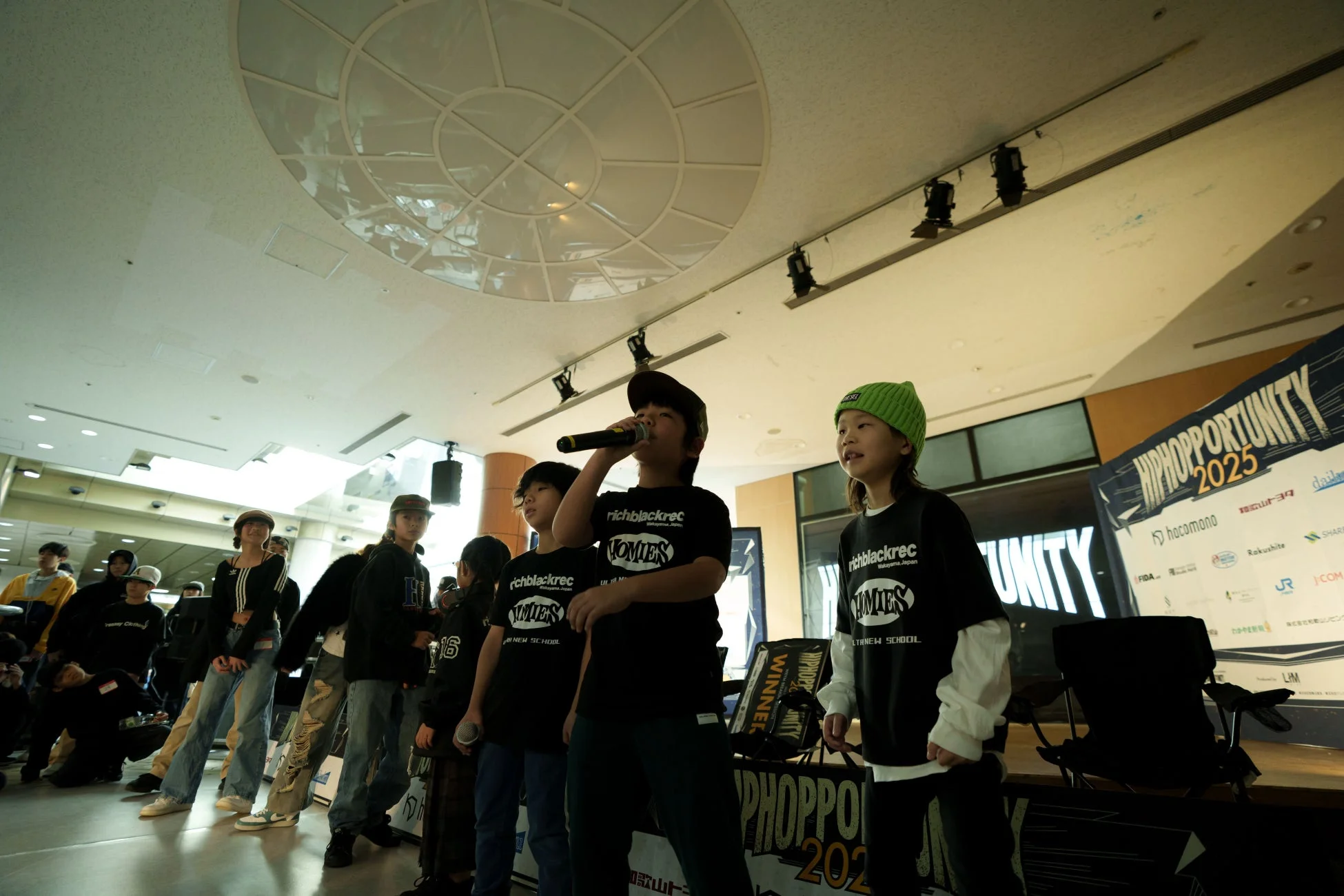 和歌山で開催されたヒップホップイベント「HIPHOPPORTUNITY 2025」で、若いパフォーマーたちがステージ上でマイクを手にパフォーマンスを披露している様子を捉えた一枚