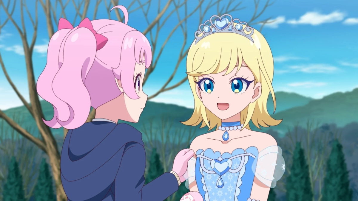 ピンク髪の少女が青いドレスとティアラを身につけた金髪の少女に優しく話しかけているアニメのワンシーン。