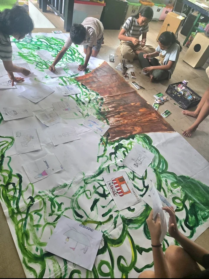 床に広げた大きな紙に子供たちが絵を描いている。共同でアートプロジェクトに取り組む創造的な活動の様子。