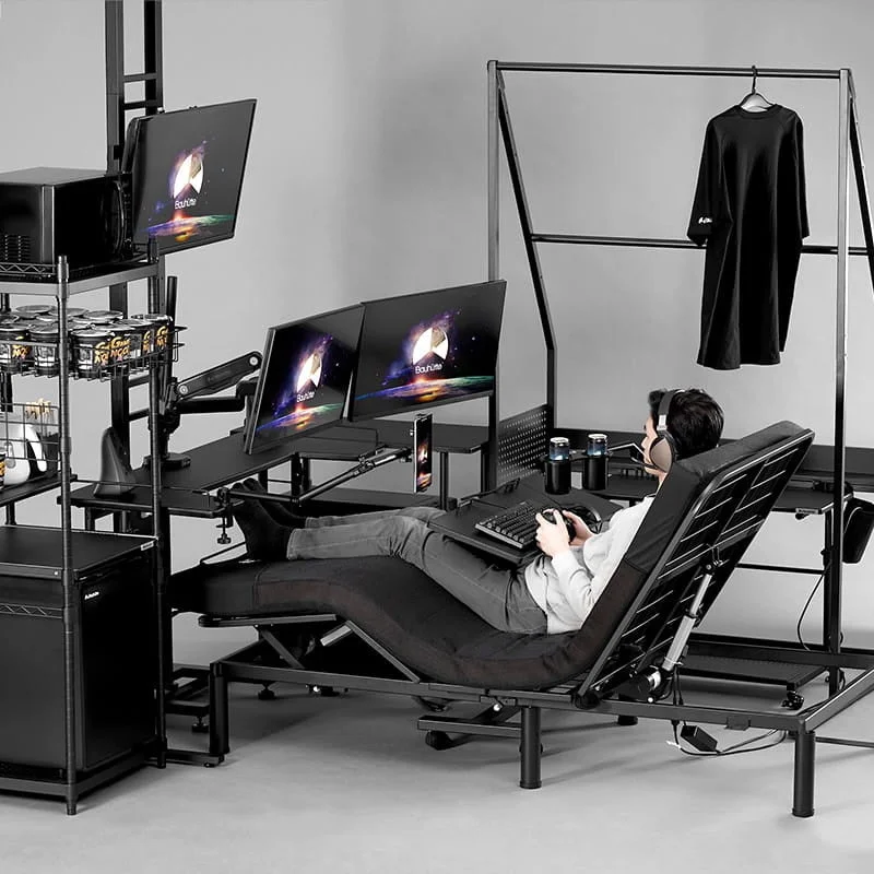 男性がリクライニングチェアに座り、複数のモニターでゲームをしている様子です。棚やハンガーラックも備わった、快適で多機能なゲーミング環境が整えられています。