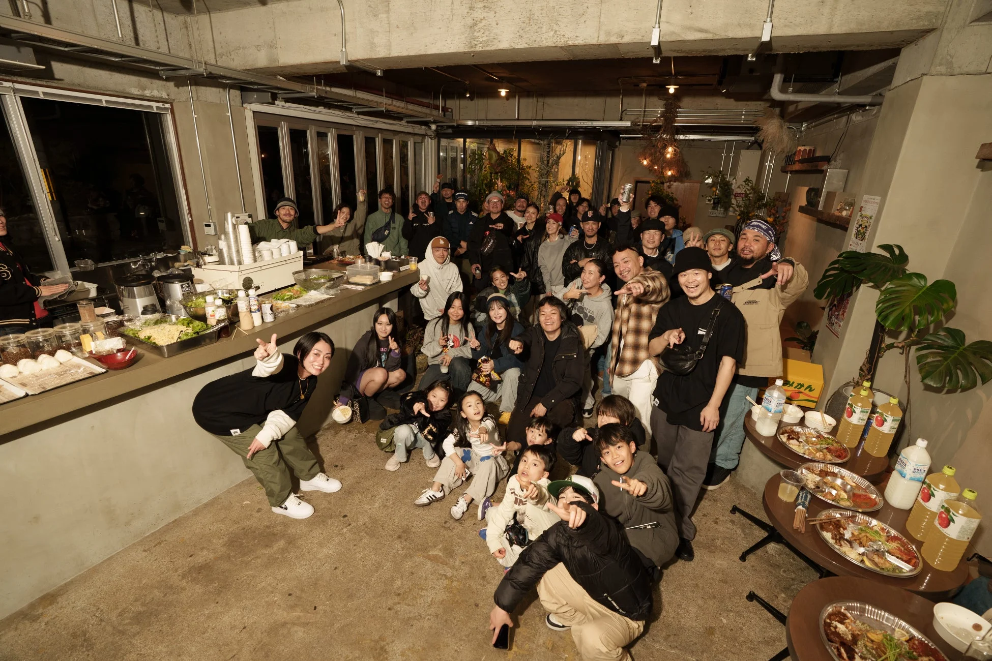 大人と子供を含む多くの人々が屋内で集まり、食事を囲んで楽しんでいる様子