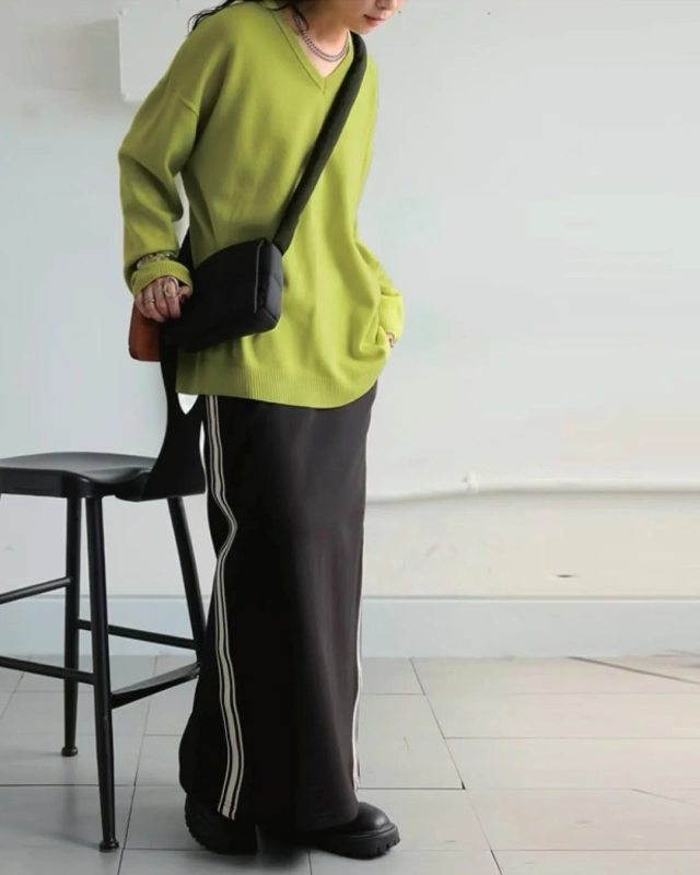 ライムグリーンのVネックニットに黒いサイドラインロングスカートを合わせた、カジュアルながらもスタイリッシュなコーディネート