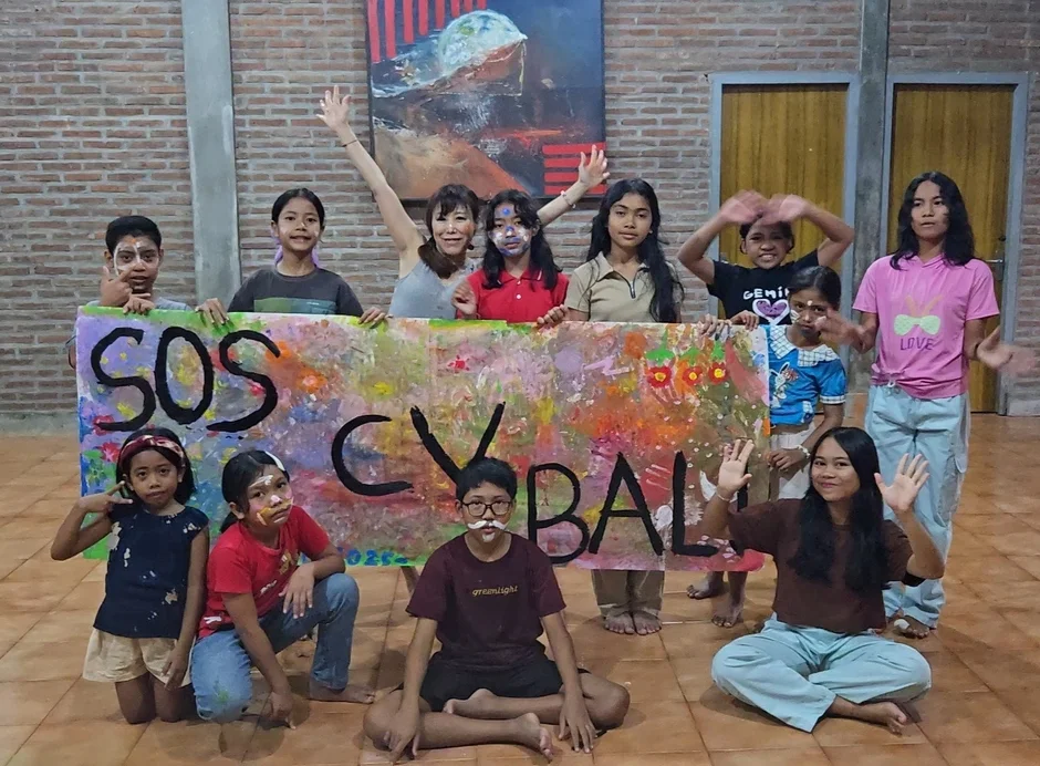 顔にペイントを施した子供たちと大人のグループが、カラフルに描かれた「SOS CYBAL」と書かれたバナーを持ってポーズをとっています。皆で楽しんでいる様子が伝わります。