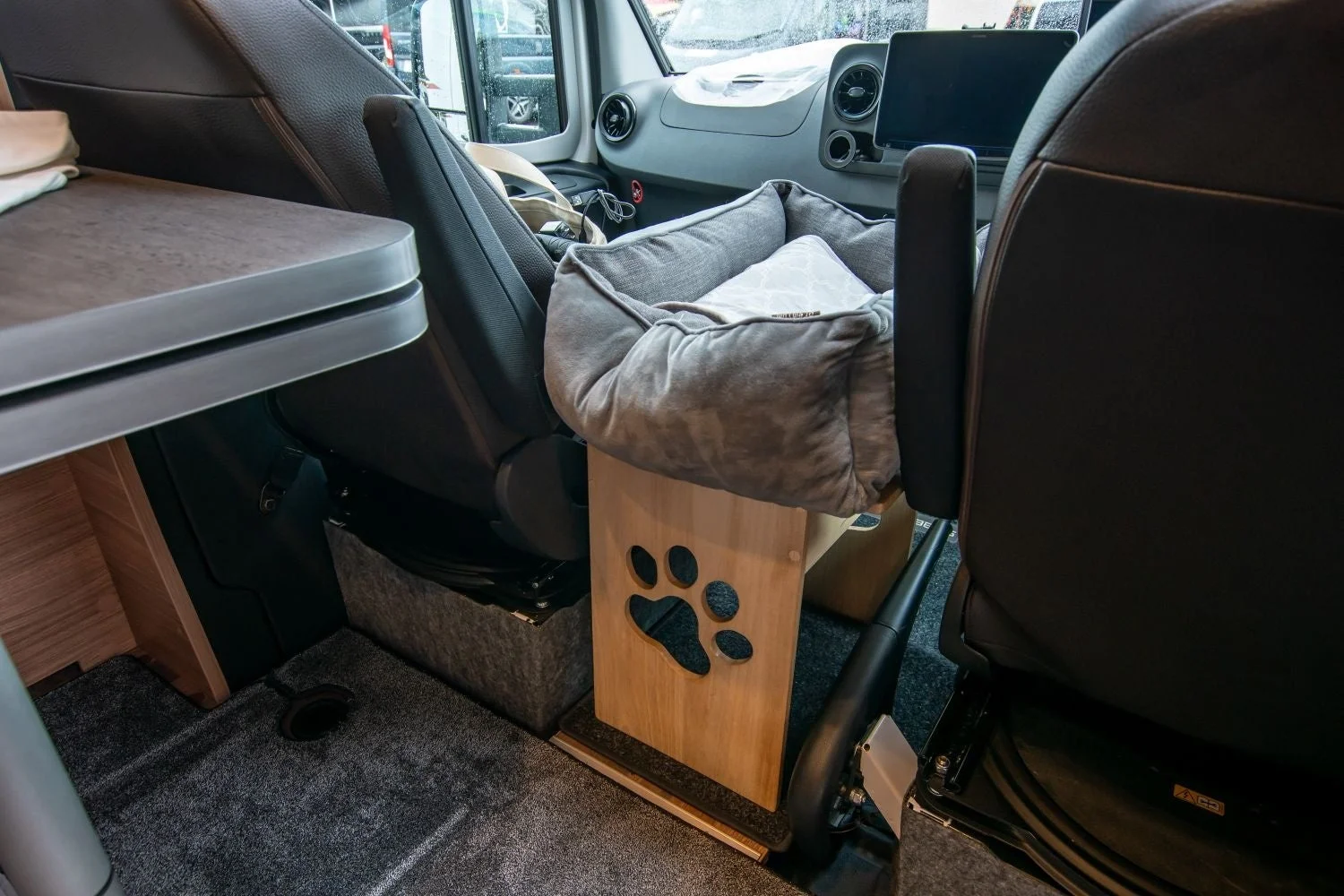 キャンピングカーの車内風景で、助手席の横に犬や猫などのペット用の快適なベッドが設置されています。ベッドの下の木製スタンドには可愛らしい足跡の切り抜きがあり、ペットとの旅行を意識した内装がうかがえます。