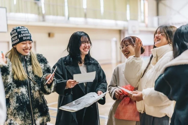 体育館のような屋内で、数人の若い女性たちが楽しそうに笑いながら交流している様子