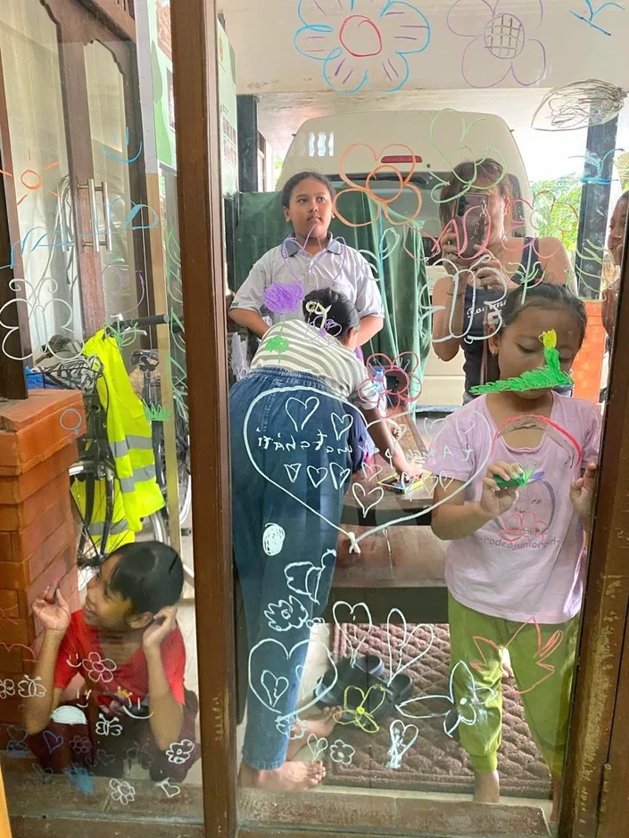 子供たちがガラスの窓にカラフルなペンで絵を描いています。花やハートなど様々なモチーフを描き、屋内で楽しそうに遊ぶ様子が映し出されています。