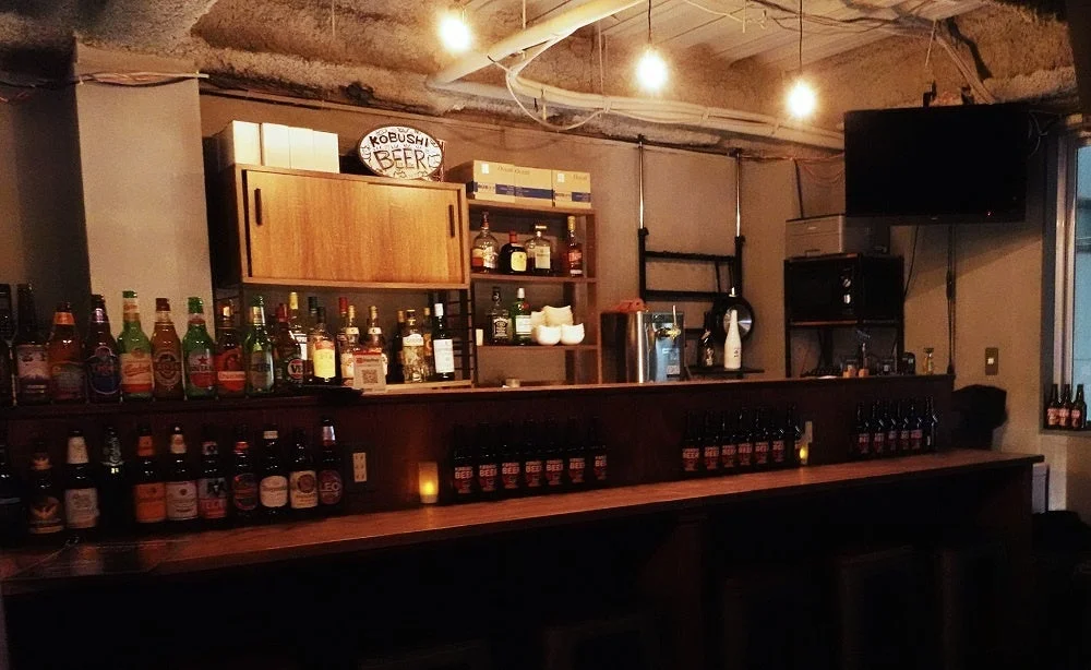 薄暗い照明のバーの店内風景でKOBUSHI BEERの看板やボトルが並ぶ