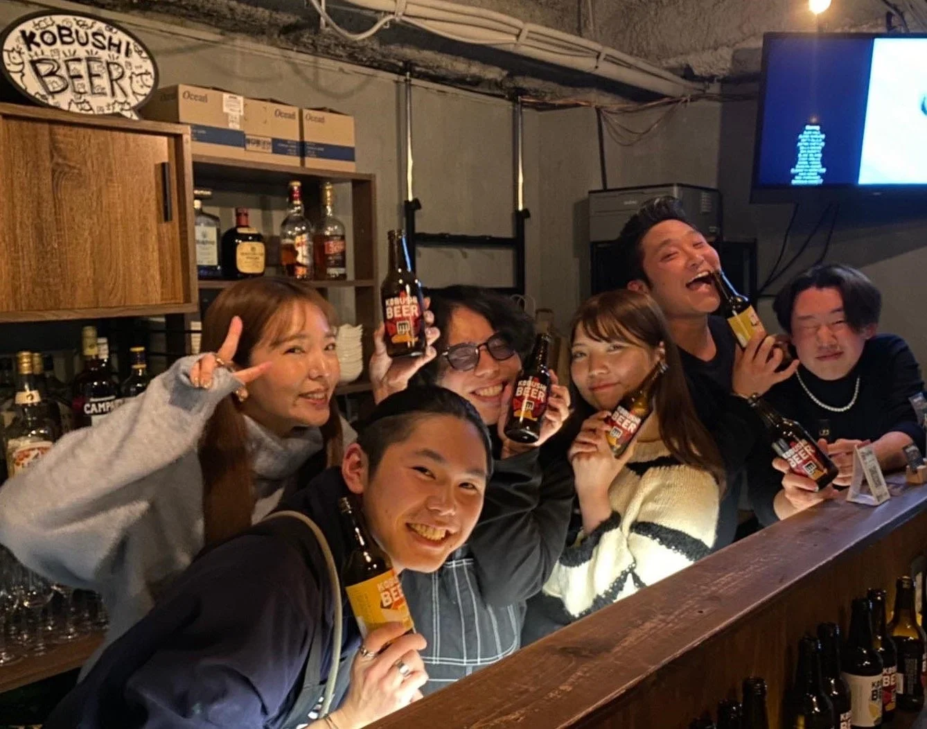 バーのカウンターで友人たちがKOBUSHI BEERのボトルを手に笑顔で写っている写真